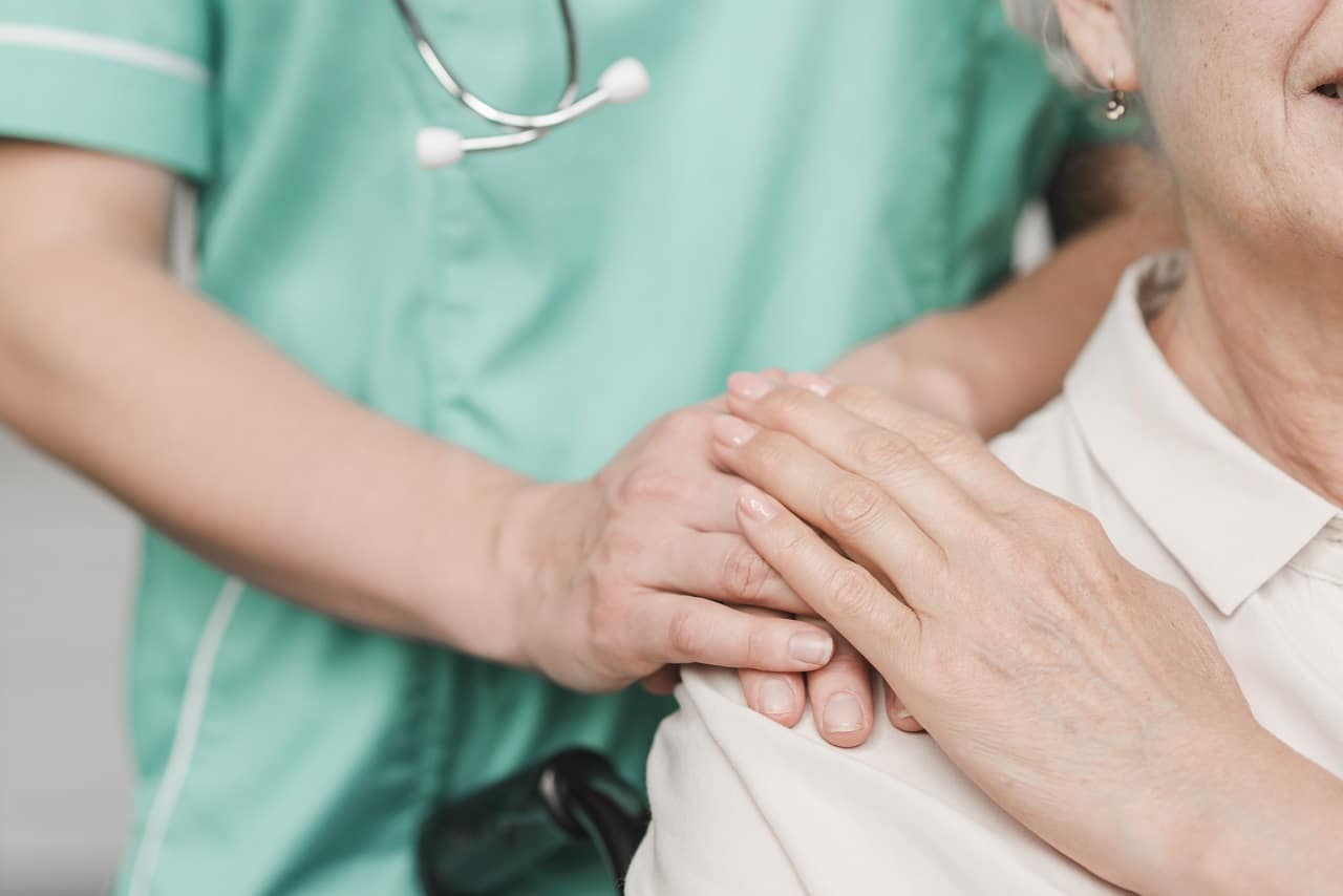 Senior woman patient touching health care giver's hands on her shoulder